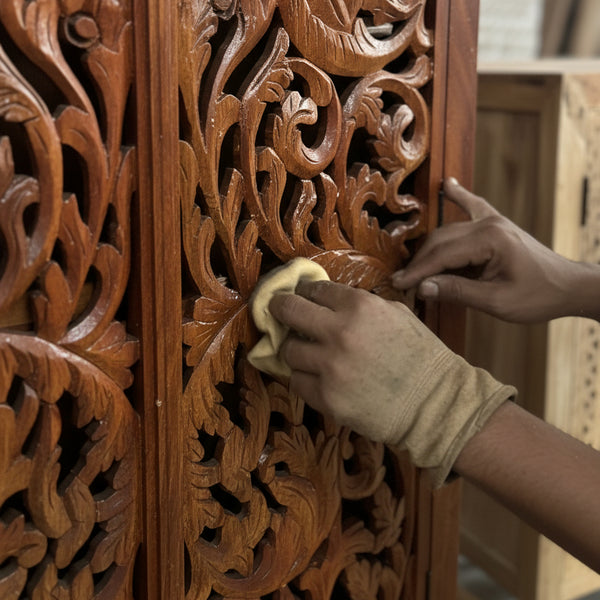Hand polishing carved wooden panel with intricate tribal floral design