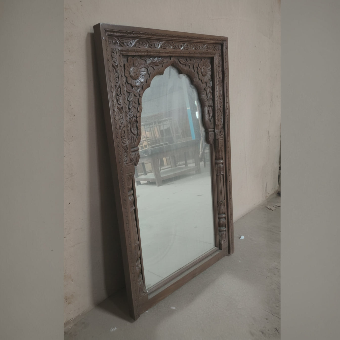 Handcrafted wooden mirror with intricate floral carvings, leaning against a wall