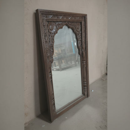 Handcrafted wooden mirror with intricate floral carvings, leaning against a wall