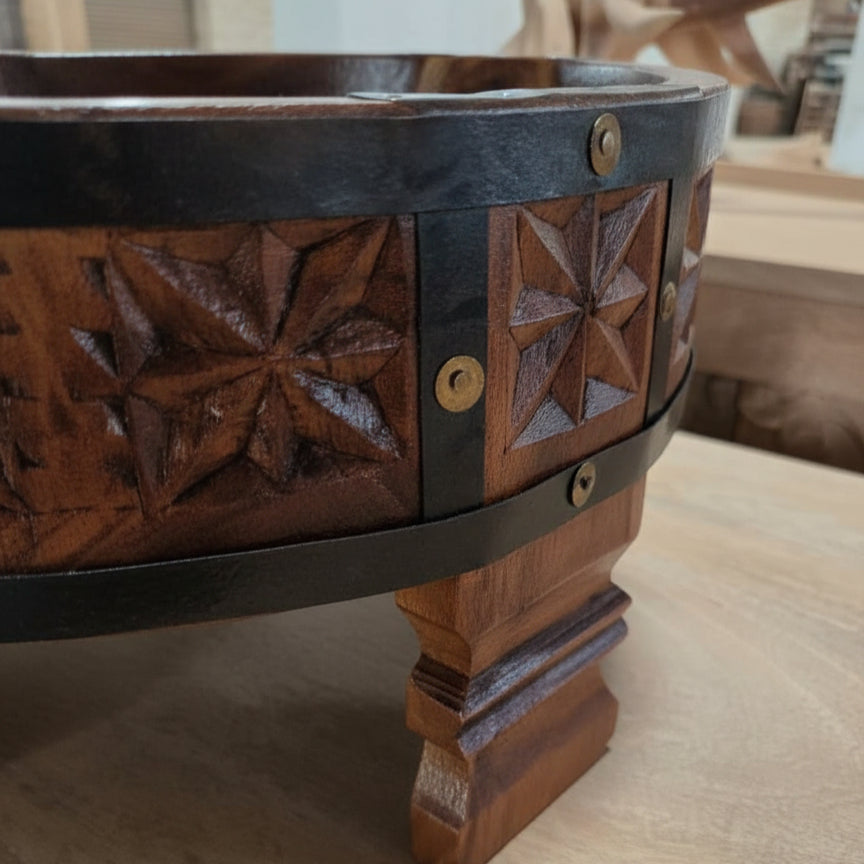 Close-up of the carved wooden detail and metal accents on the leg of an Ahaar Wooden Fruit Bowl showcasing intricate tribal handicraft decor.