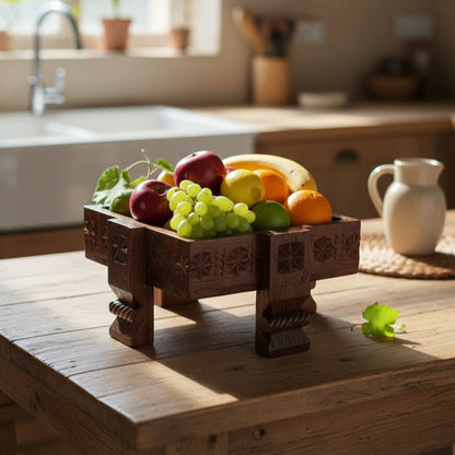 Ahaar Wooden Fruit Bowl crafted from wood with carved patterns, filled with fresh fruits including apples, grapes, bananas, lemons, and placed on a rustic wooden table in a kitchen setting.