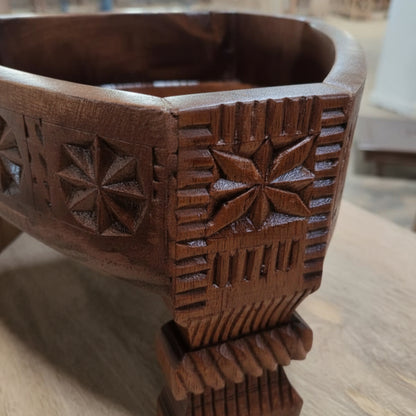 Close-up of hand-carved wooden decor featuring intricate tribal patterns on the leg of an Ahaar Wooden Fruit Bowl made from dark polished wood.