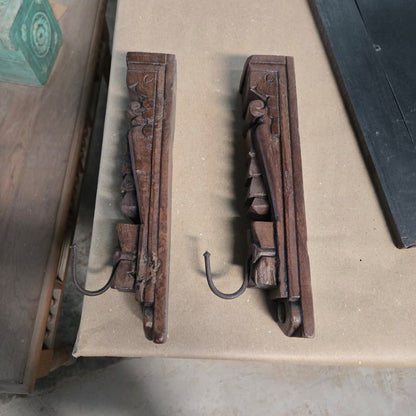Introducing the Ankush Coat Hooks: a set of two carved wooden wall hooks featuring ornate geometric and floral details, showcased on a beige surface. Each hook is crafted with exquisite attention to detail and includes a sturdy metal hanger extending from the base, making them an elegant handcrafted decor accent for any space.