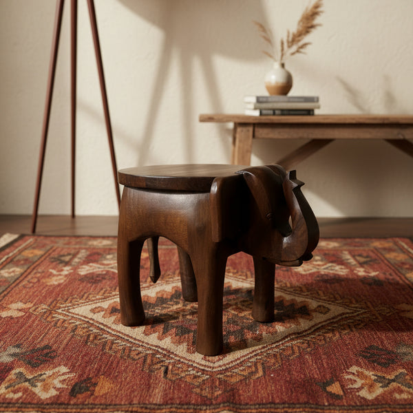 Handcrafted wooden elephant stool on patterned tribal rug in rustic living room setting