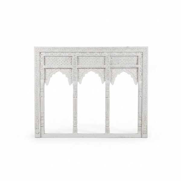 The Jharokha Wall Hanging is an ornate white carved wooden frame featuring three arches with intricate patterns and detailed columns, inspired by traditional architectural designs. Set against a plain white background, this stunning piece of handicraft is perfect for adding sophisticated decor to any space.