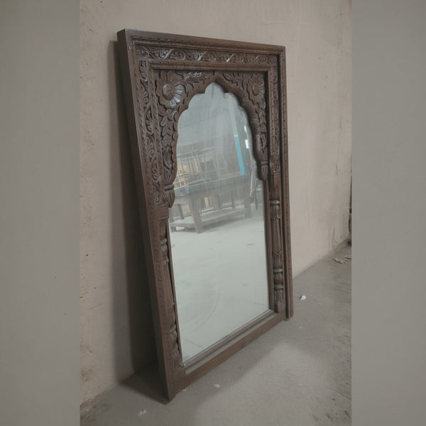 Handcrafted wooden mirror with intricate floral carvings, leaning against a wall