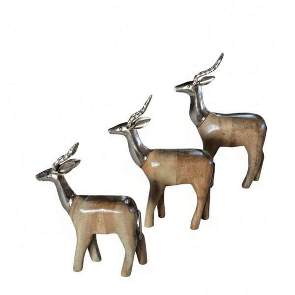 The Mriga Trio Wooden Decor features three polished wooden deer figurines with metallic silver antlers, arranged together and facing left. Combining natural wood with metallic accents, this set adds a charming touch to any decor.