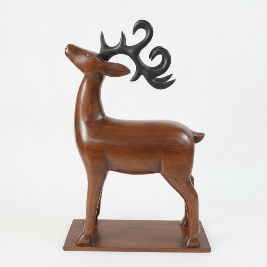 The Mriga Wooden Deer Sculpture features a smooth, upward-tilting head with black, stylized antlers and stands gracefully on a rectangular wooden base against a plain white background—an elegant decor piece that beautifully highlights fine wooden craftsmanship.