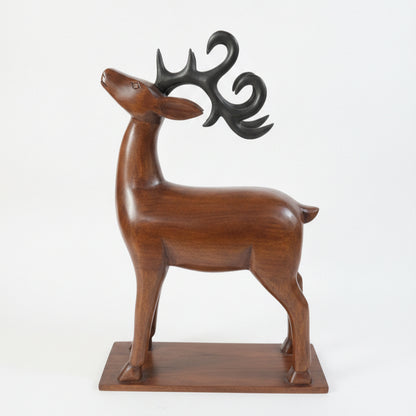 The Mriga Wooden Deer Sculpture features a smooth, upward-tilting head with black, stylized antlers and stands gracefully on a rectangular wooden base against a plain white background—an elegant decor piece that beautifully highlights fine wooden craftsmanship.
