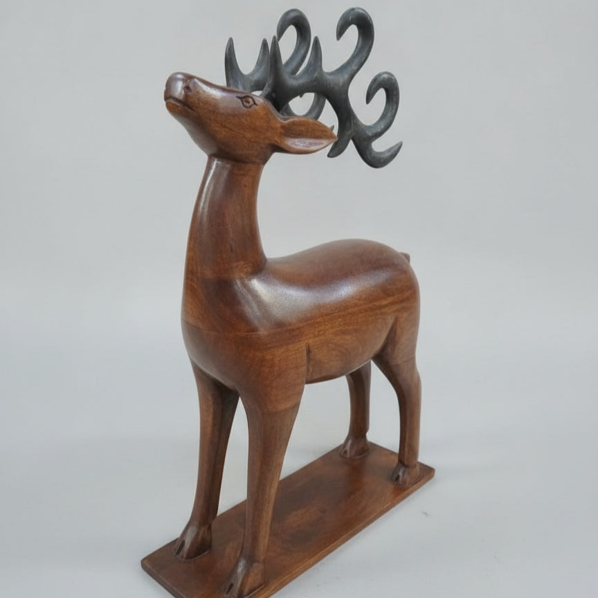 The Mriga Wooden Deer Sculpture features a stylized deer with curly antlers standing on a rectangular base against a plain, light background, making it an elegant decor piece.
