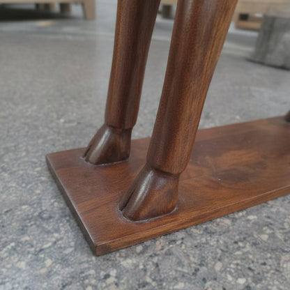 Close-up of the Mriga Wooden Deer Sculpture—a striking decor piece featuring two intricately handcrafted wooden legs, artfully shaped like deer legs and set upon a polished rectangular wooden base, displayed on a gray textured floor.