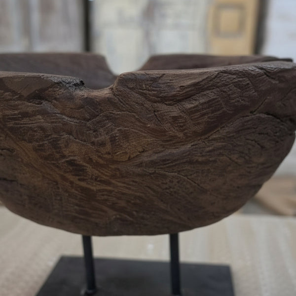 Close-up of a rustic wooden handcrafted bowl with textured grain patterns displayed on a black metal stand, showcasing the Prakriti Root Bowl Decor.