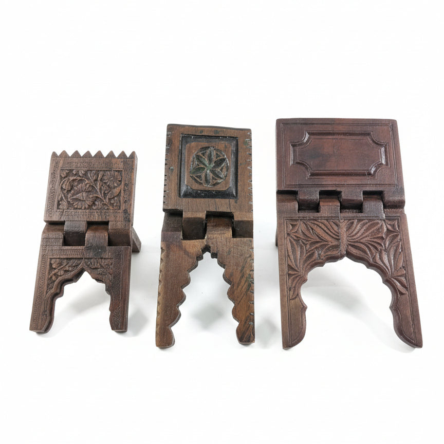 Three intricately carved Rehal Wooden Carved Bookstands made of dark wood, each featuring unique floral and geometric patterns, perfect for traditional decor or handicraft displays.