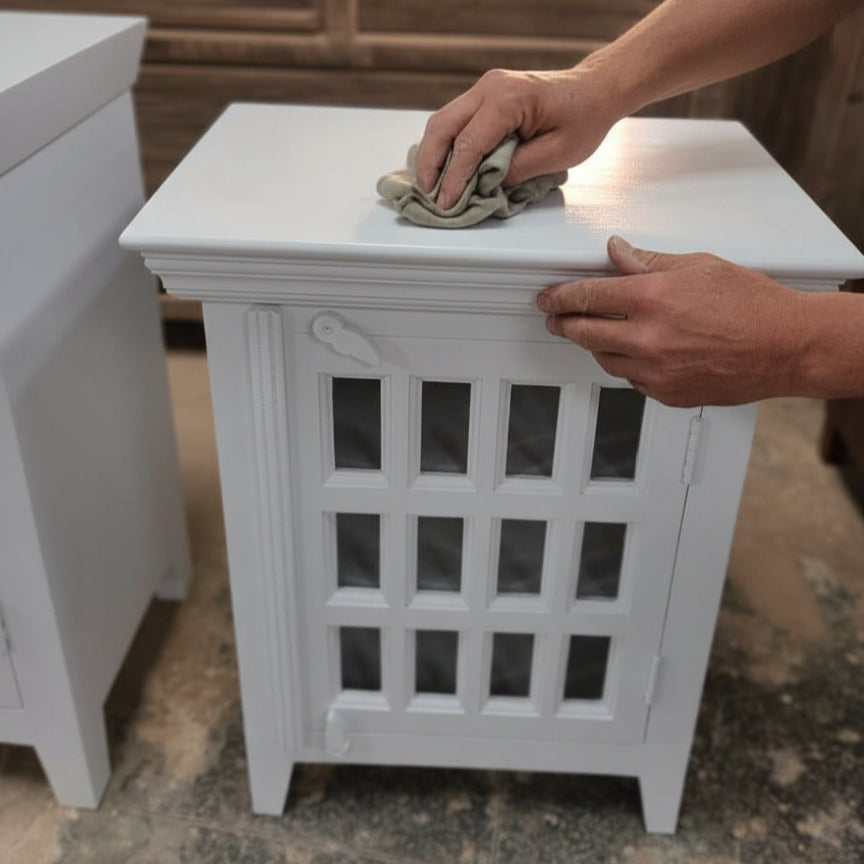 Handcrafted white wooden cabinet with glass-paneled door being polished by hand