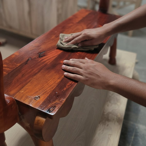 Close-up of hands polishing the rich wooden surface of the Vahana Carved Wooden Bench, highlighting its smooth finish and detailed craftsmanship.