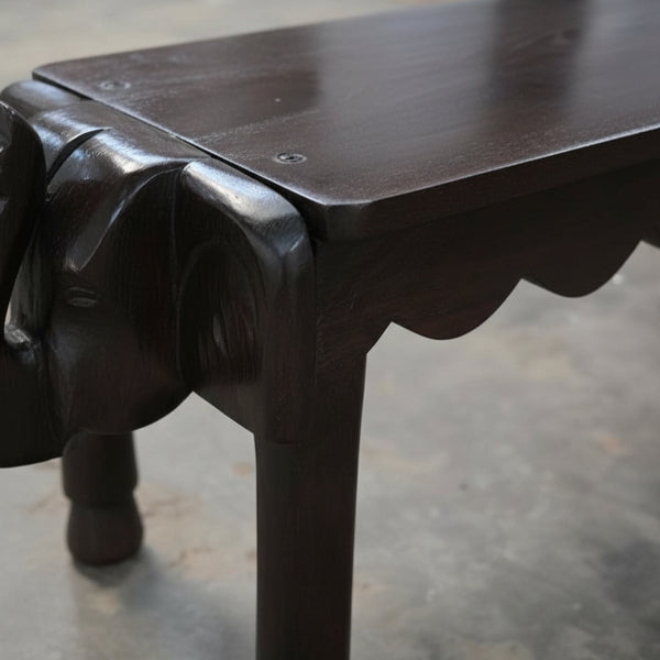 Vahana Carved Wooden Bench featuring a dark polished wood finish with detailed elephant head carvings on the legs, showcasing tribal handicraft decor artistry.