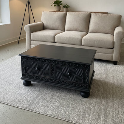 Yantra Storage Coffee Unit featuring dark wooden handcrafted design with intricate tribal patterns, placed in a modern living room with a beige sofa and neutral decor.